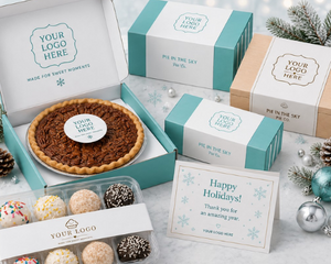 A styled holiday gift set of assorted pastries and pies in branded packaging. The set includes a whole pie tart in an open box, a boxed assortment of truffles, a 'Happy Holidays' greeting card, and several closed gift boxes and cartons in teal and kraft paper with placeholder branding.